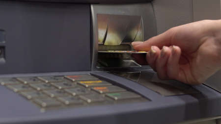A young woman inserts a bank card into an ATM. ATM for cash withdrawal and deposit. Womans hand close-up.の写真素材