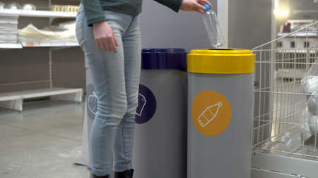 A young woman throws a plastic bottle into the trash. Special containers for sorting garbage. Container for plastic.の写真素材