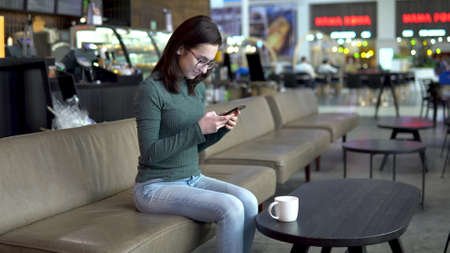 A young woman is sitting in a cafe with a phone. The girl is in correspondence on a smartphone. Close-up.の写真素材