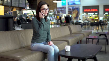 A young woman is sitting in a cafe and talking on the phone. A girl is talking on the phone.の写真素材
