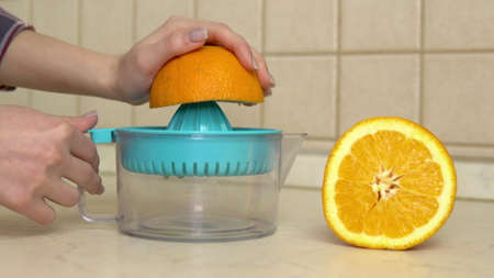 A woman squeezes juice from an orange. A woman uses a juicer. Hands close up.の写真素材