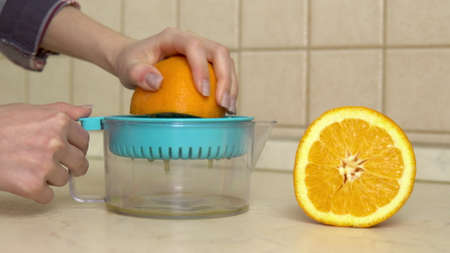 A woman squeezes juice from an orange. A woman uses a juicer. Hands close up.の写真素材