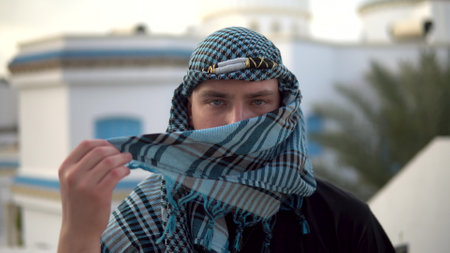 Young man in arabic handkerchief. The man covers his face. Against the background of the Arab house.の写真素材