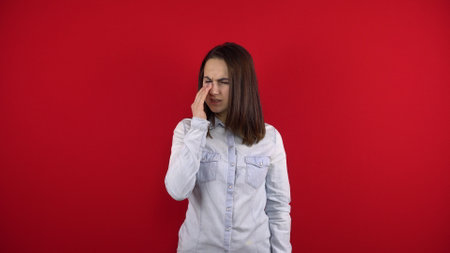 The young woman has a sore nose, she touches it with her hand. Shooting on a red background.の写真素材