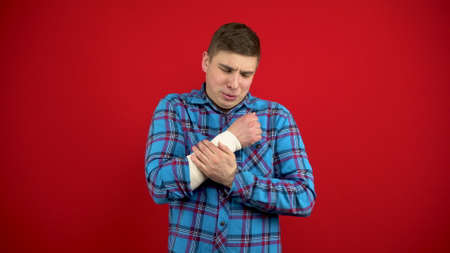 The young man has a bandaged hand. A man touches a sore hand. Shooting on a red background.の写真素材