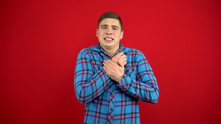 A young man has a sore arm. The man touches the sore hand. Shooting on a red background.の写真素材