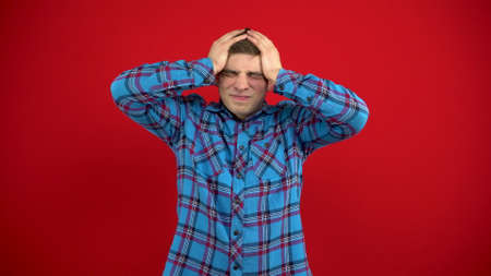 A young man has a headache and holds it in his hands. Shooting on a red background.の写真素材