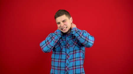 The young man has a sore nose, he touches it with his hand. Shooting on a red background.の写真素材