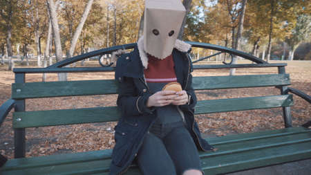 The girl with the package on her head is sitting on a bench with a cheeseburger. Girl in a jacketの写真素材