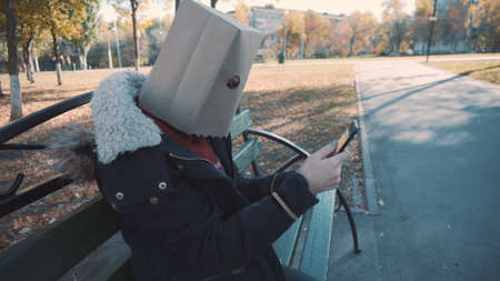 The girl with the package on his head is sitting on a bench with a phone. Girl in a jacketの写真素材