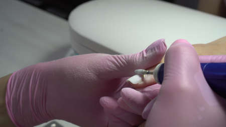 Young woman in the salon does a manicure. A manicurist uses a drill machine to remove nails....