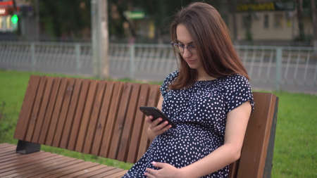 Young pregnant girl with a phone in her hands. A girl with glasses and a dress is texting on the phone.の写真素材