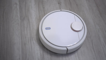 A white robot vacuum cleaner rides on a white parquet floor. The robot with artificial intelligence determines the space and cleans the floor.の写真素材