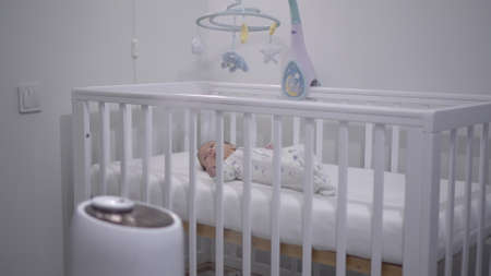 A newborn baby lies in a crib against the background of an ultrasonic humidifier.の写真素材
