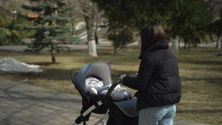 A young mother gulet in the park with a baby in a stroller. Woman and child in jackets.の写真素材