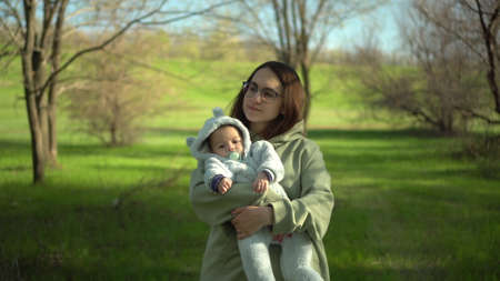 A young mother walks with a baby in nature. A girl with glasses holds a child in her arms. Closeup.の写真素材
