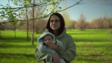 A young mother walks with a baby in nature. A girl with glasses holds a child in her arms. Closeup.の写真素材