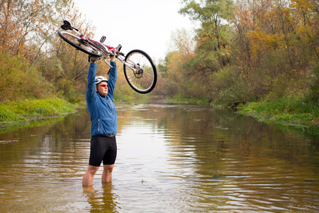 Young athlete crossing rocky terrain with bicycle in his handsの写真素材