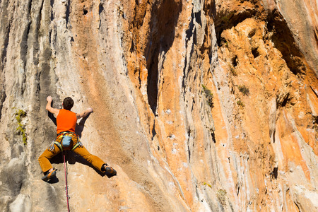 Young male climber hanging by a cliff.