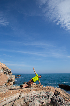 fitness, sport, people and lifestyle concept - young man making yoga exercises on beach from backの写真素材