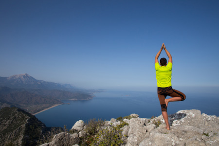 fitness, sport, people and lifestyle concept - young man making yoga exercises on beach from backの写真素材