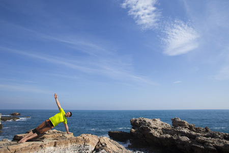 fitness, sport, people and lifestyle concept - young man making yoga exercises on beach from backの写真素材