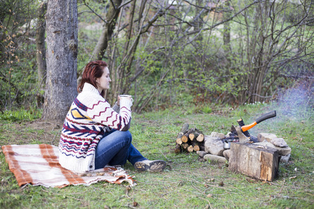 Girl sitting near a campfire at the campsite looking at map and drinking coffee.の写真素材