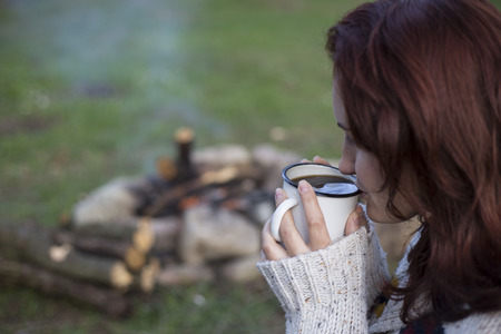 Girl sitting near a campfire at the campsite looking at map and drinking coffee.の写真素材