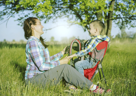 Mother with baby in backpack carrier is hiking in mountains. Tourist is carrying a child on his back on the nature.の写真素材
