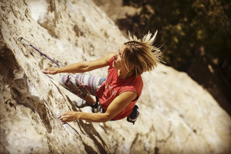 Woman rock climber. Rock climber climbs on a rocky wall. Woman makes hard move.の写真素材