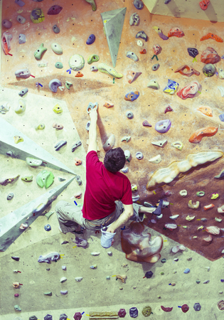 Young man practicing rock-climbing on a rock wall indoors.の写真素材