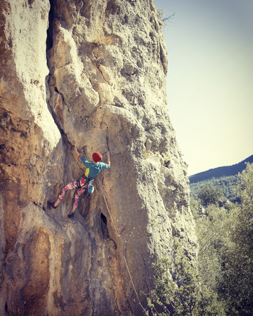Woman rock climber. Rock climber climbs on a rocky wall. Woman makes hard move.の写真素材