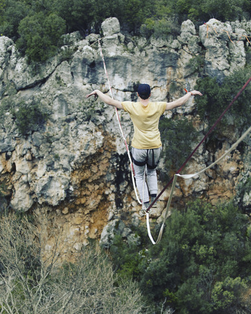 A man is walking along a stretched sling. Highline in the mountains. Man catches balance....