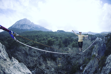 A man is walking along a stretched sling. Highline in the mountains. Man catches balance....