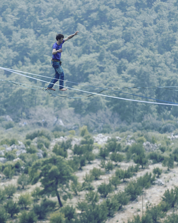 A man is walking along a stretched sling. Highline in the mountains. Man catches balance....