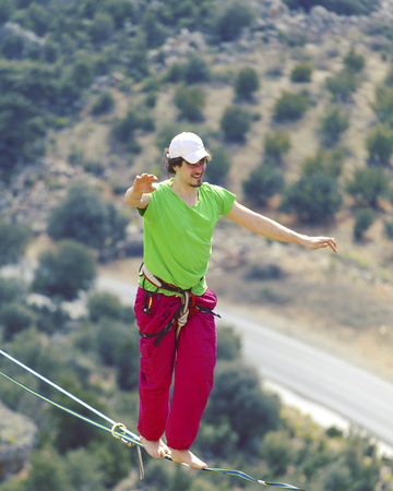 A man is walking along a stretched sling. Highline in the mountains. Man catches balance....