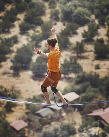 A man is walking along a stretched sling. Highline in the mountains. Man catches balance....
