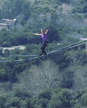 A woman is walking along a stretched sling. Highline in the mountains. Woman catches balance. Performance of a tightrope walker in nature.の写真素材