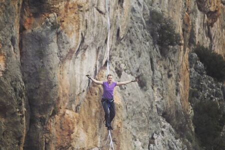 A woman is walking along a stretched sling. Highline in the mountains. Woman catches balance. Performance of a tightrope walker in nature.の写真素材