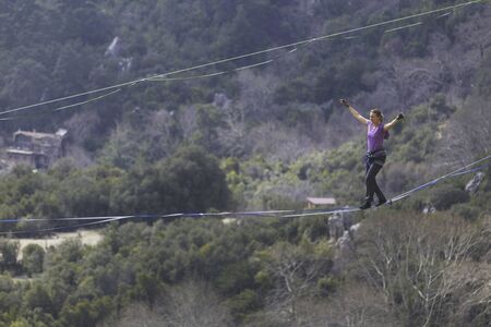 A woman is walking along a stretched sling. Highline in the mountains. Woman catches balance....