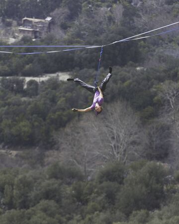 A woman is walking along a stretched sling. Highline in the mountains. Woman catches balance. Performance of a tightrope walker in nature.の写真素材