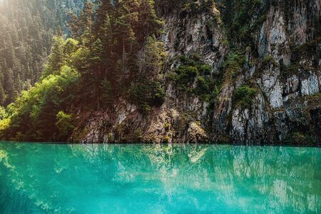 Autumn forest on a mountain slope is reflected in a pond with turquoise water.の写真素材