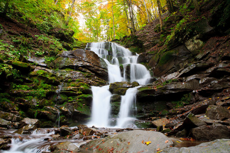 Beautiful view of the waterfall in the beech forest in the golden autumn season.