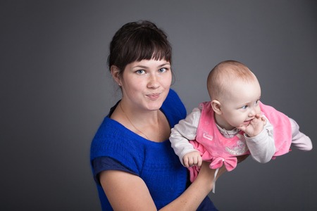 Happy mother embraces her little daughter on gray backgroundの写真素材