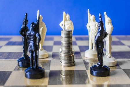 Coins are stacked on a chessboard surrounded by black and white chess pieces, the concept of leadership, the concept of businessの写真素材