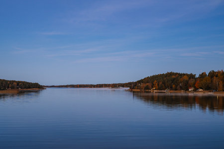 Golden sunrise over calm autumn sea with forest on the shore and gentle fog above the water, peaceful natural seascape and morning atmosphere.の写真素材