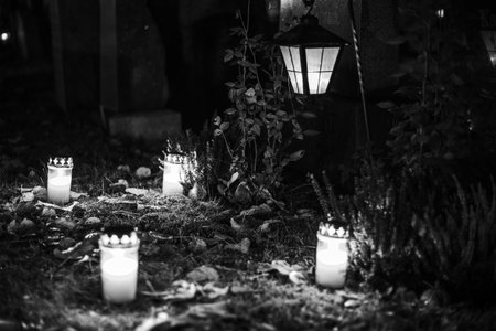 Black and white photograph of cemetery crosses and glowing lanterns, soft candlelight creating a...