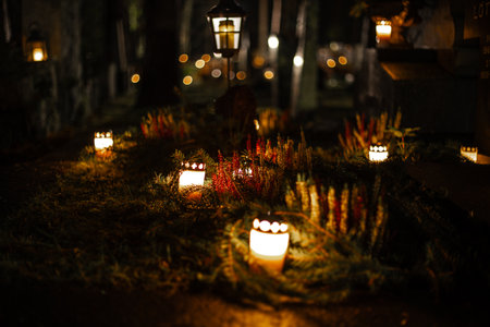 Lit candles on a cemetery at night, warming flames creating a calm and emotional memorial atmosphere among graves.の写真素材