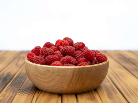 Fresh raspberries in wooden bowl on wooden background. With copy space for text.