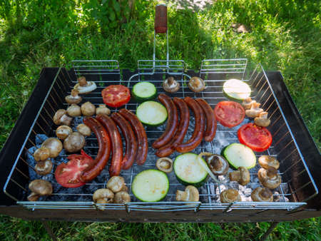 Roasting on the grill. Fried sausages and vegetables on the grill outdoors. BBQ. Fried food is fried and smoked on charcoal grills. It turns out a grill with delicious tasty sausages, vegetables.の写真素材